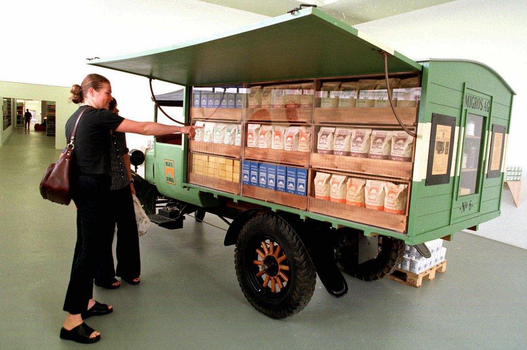 Due signore osservano e commentano un camioncino d epoca caricato con finte confezioni di 5 prodotti alimentari