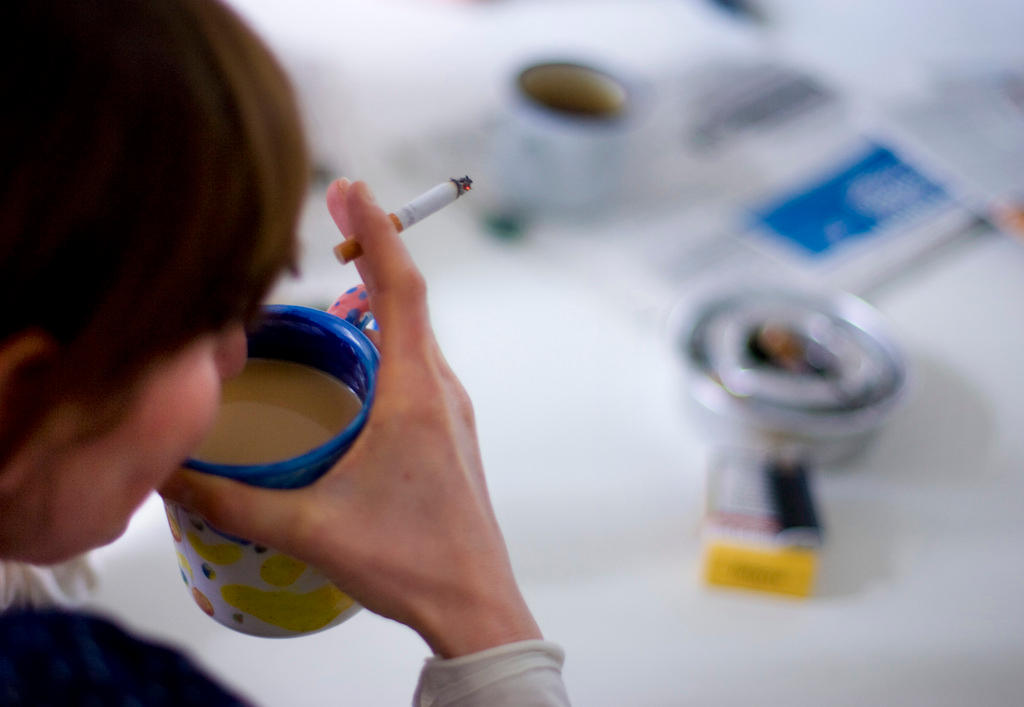 A woman smokes a cigarette and drinks a cup of coffee at the office