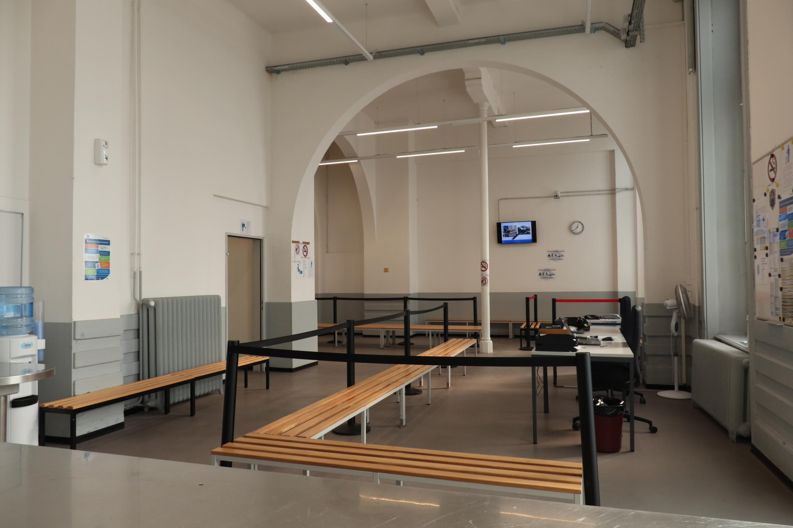 Grande stanza con lunghe panche, un distributore d acqua minerale, due scrivanie con computer