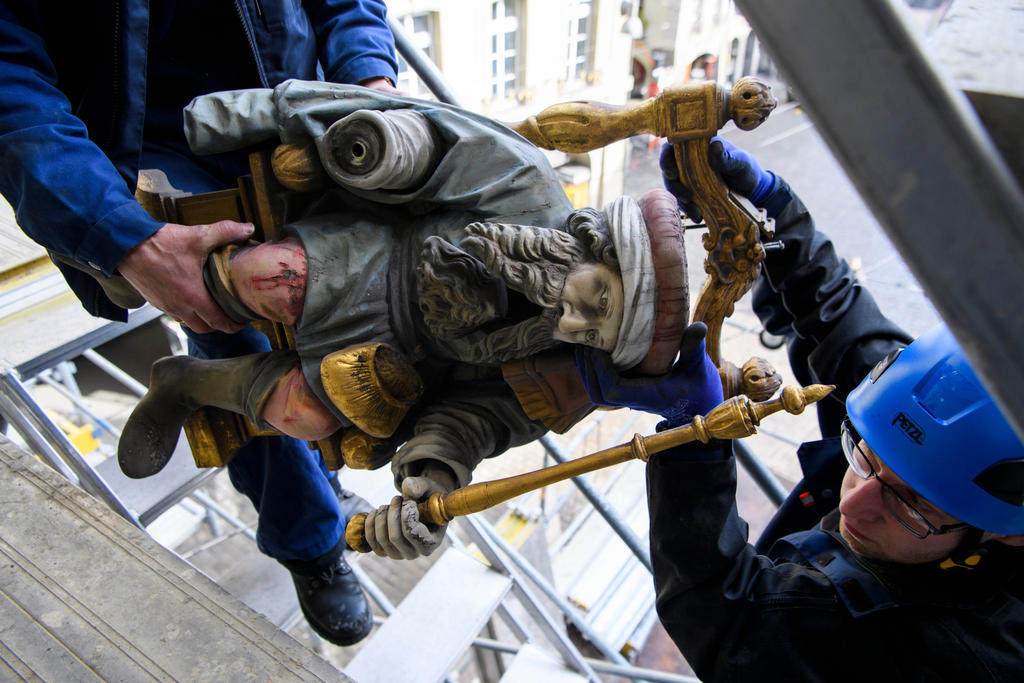 A figure Chronos, the god of time is dismantled from the Zytglogge by two workmen.