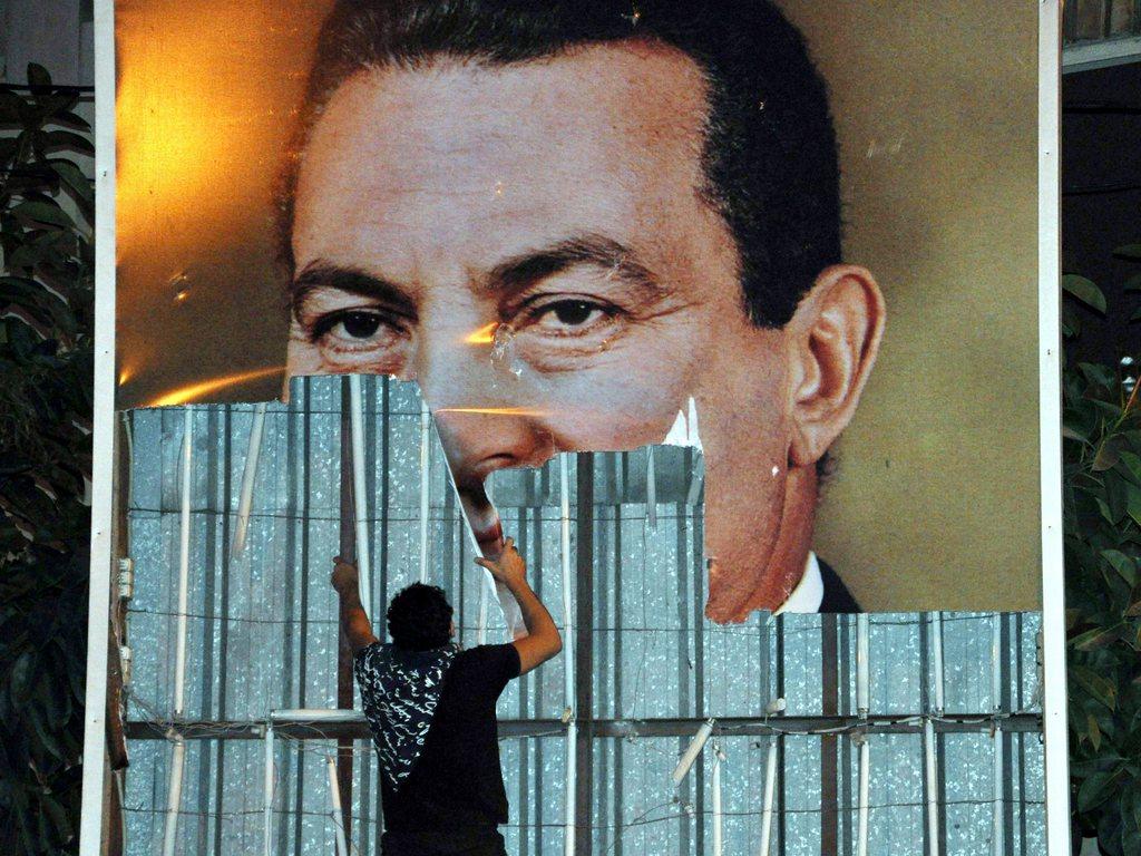 رجل يُمزق لافتة عملاقة تحمل صورة الرئيس المصري الأسبق حسني مبارك