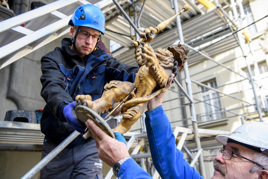 Two men wearing hard hats help lift a figure of a lion.