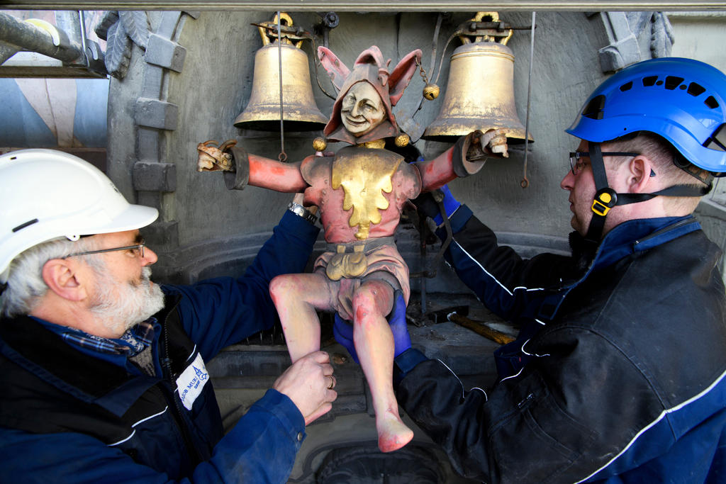 Two craftsmen demount a figure of a Joker at the face of the Zytglogge clock tower.