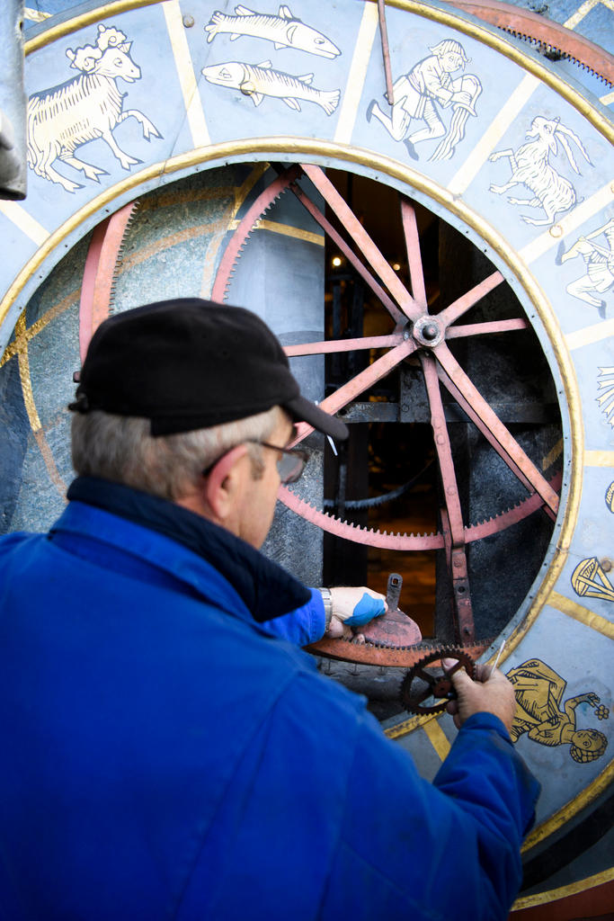 A man dressed in blue stands with his back to the camera with cogs of a clock in his hands.