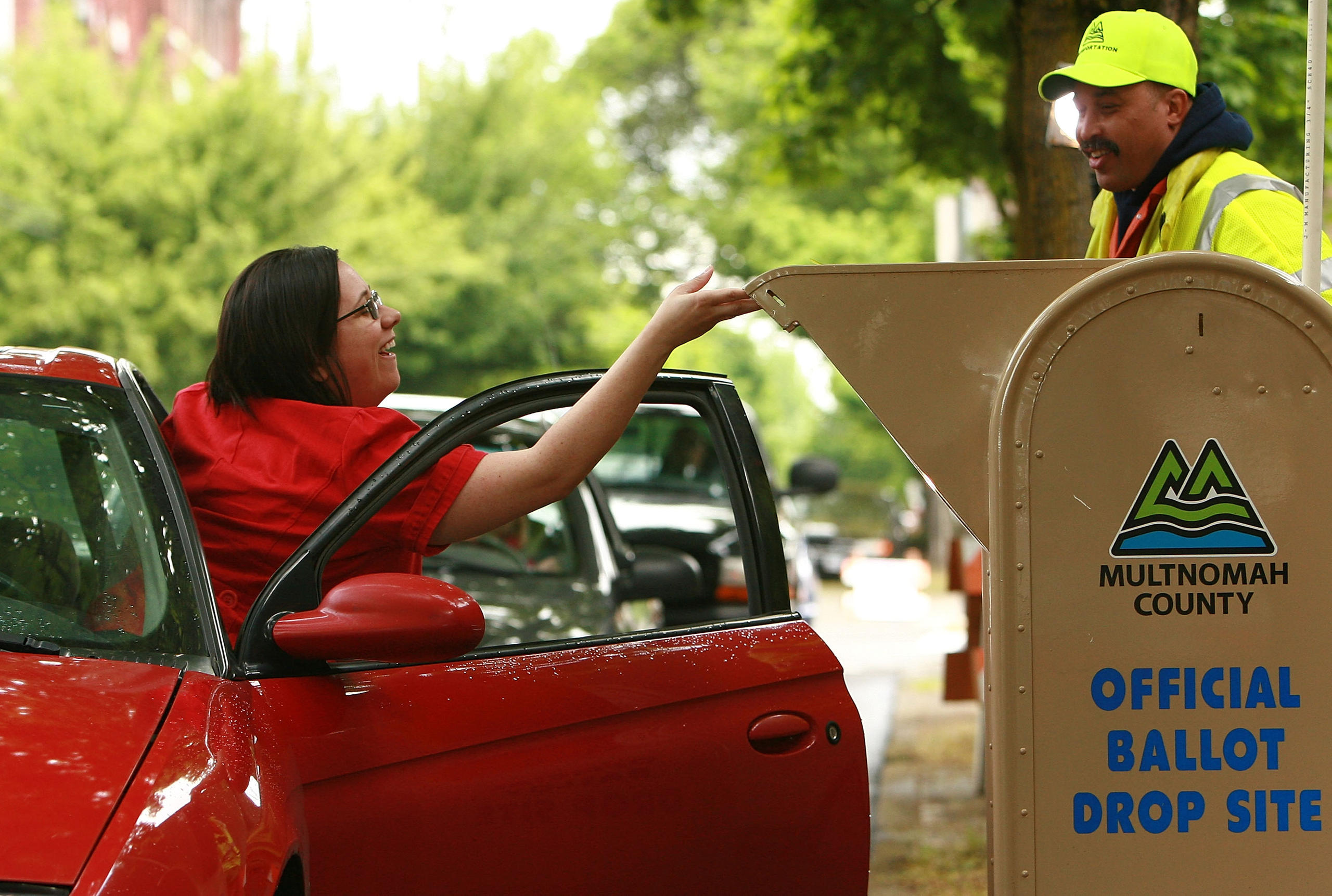 Una donna esce da un auto e mette la scheda di voto in un urna sul marciapiede.