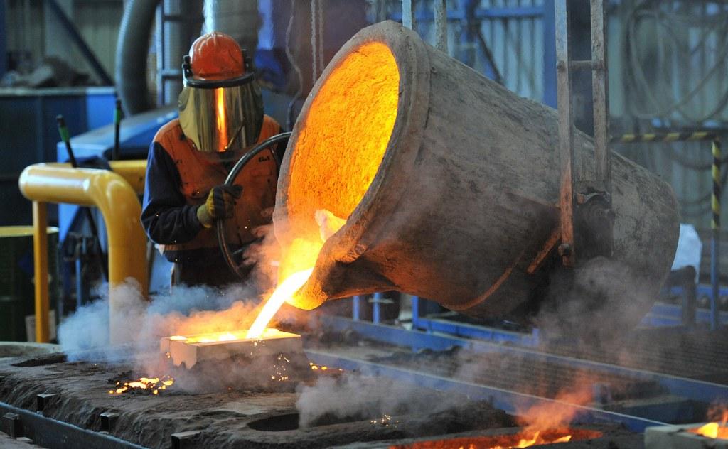 Factory worker pours molten steel into a mould
