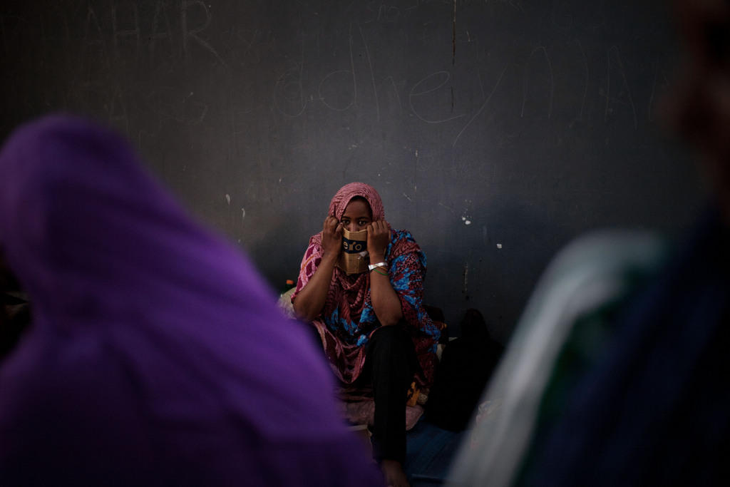 Somali woman in coloured clothes sits in Libyan detention centre