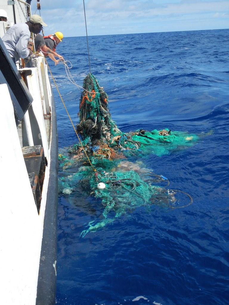 люди на корабле вытаскивают мусор из воды