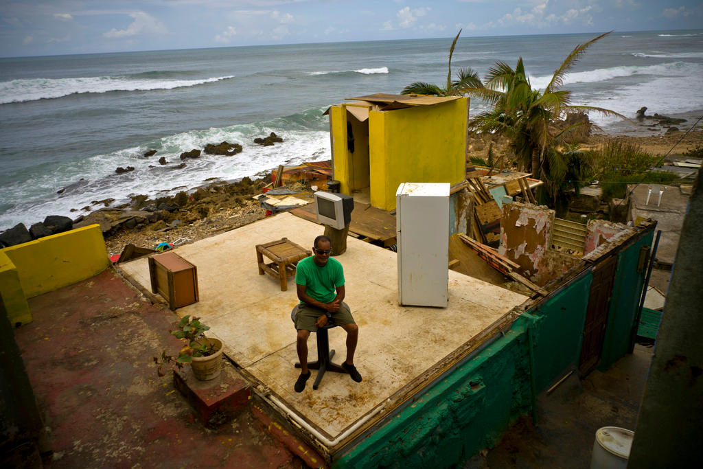 A man sits amid the ruins of a house by the sea.
