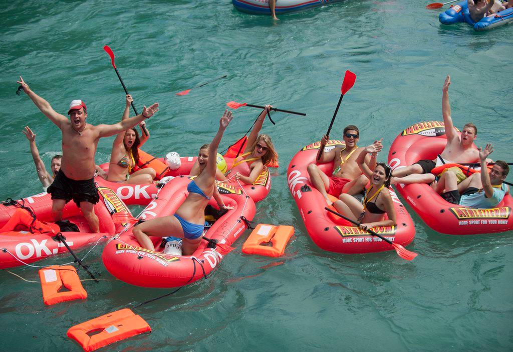 A number of waving people in swimwear in red rubber dinghies