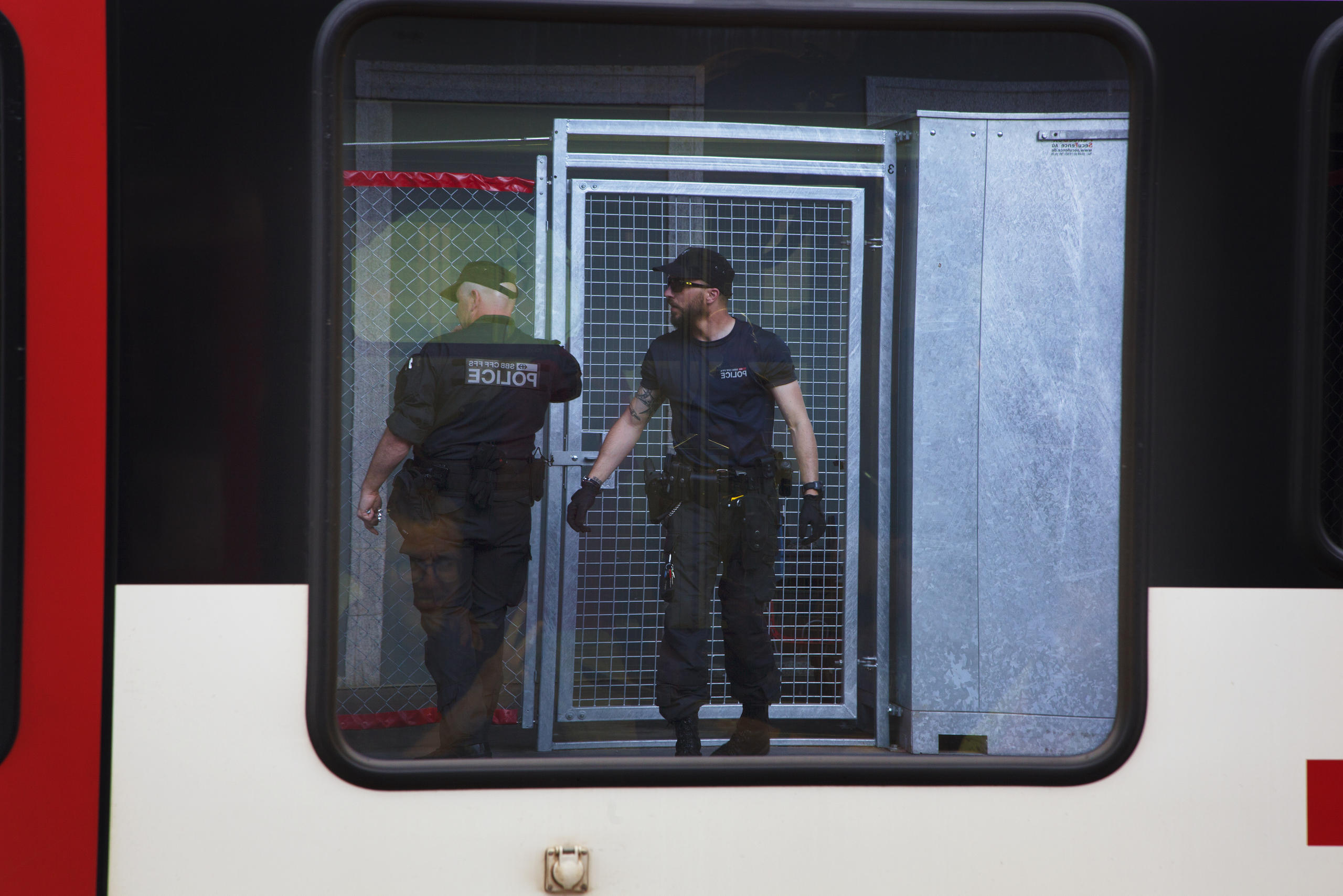 Due agenti davanti a una cella, visti specchiati sul finestrino di un treno
