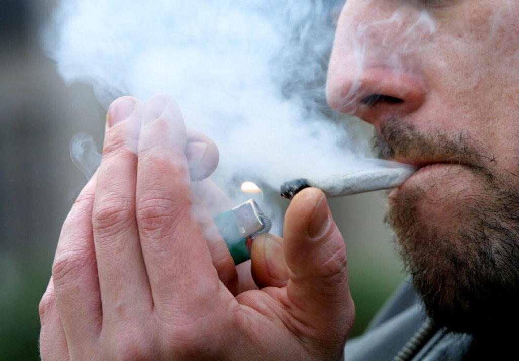 A hand holds a cigarette over a full ashtray