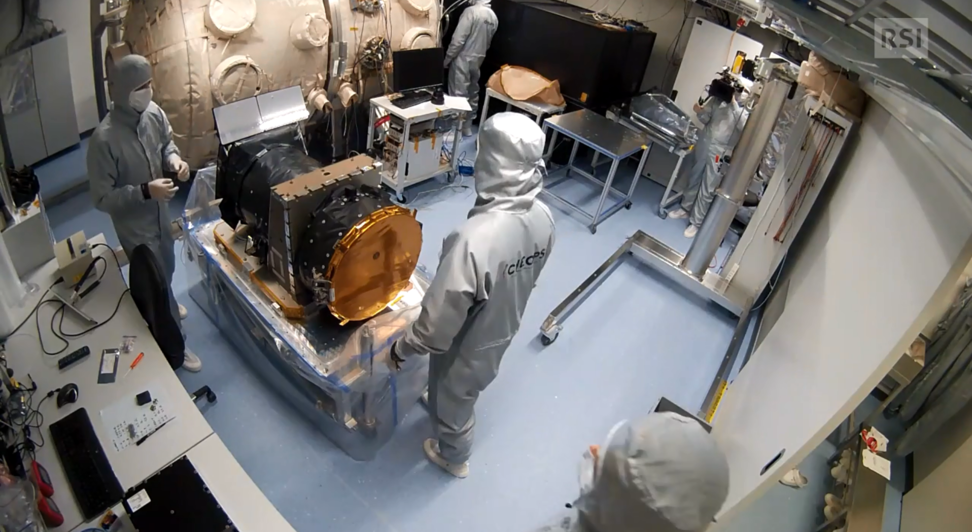 Il satellite circondato da tre scienziati vestiti di tuta, guanti e mascherina in una stanza appositamente isolata