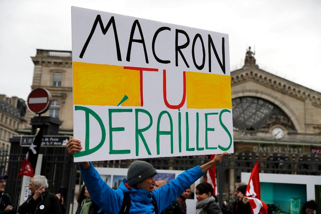 Manifestante regge cartello con la scritta: Macron tu dérailles