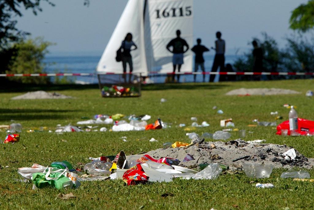 Pile of rubbish on grass in front of a lake and sailing boats