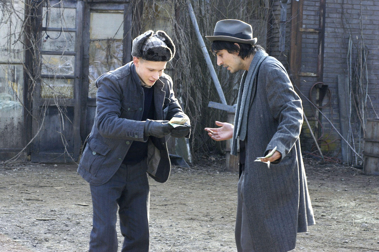 Two young men stand looking at money in the hands of the young man on hte left.