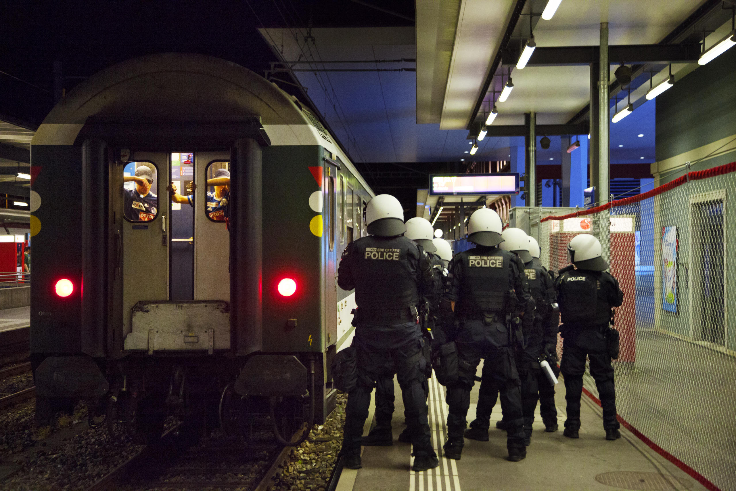 Gruppo di sette agenti in tenuta antisommossa, di schiena, accanto alla coda del treno
