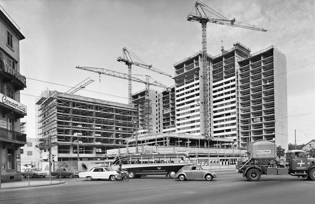 High-rise building surrounded with cranes and traffic in the foreground.