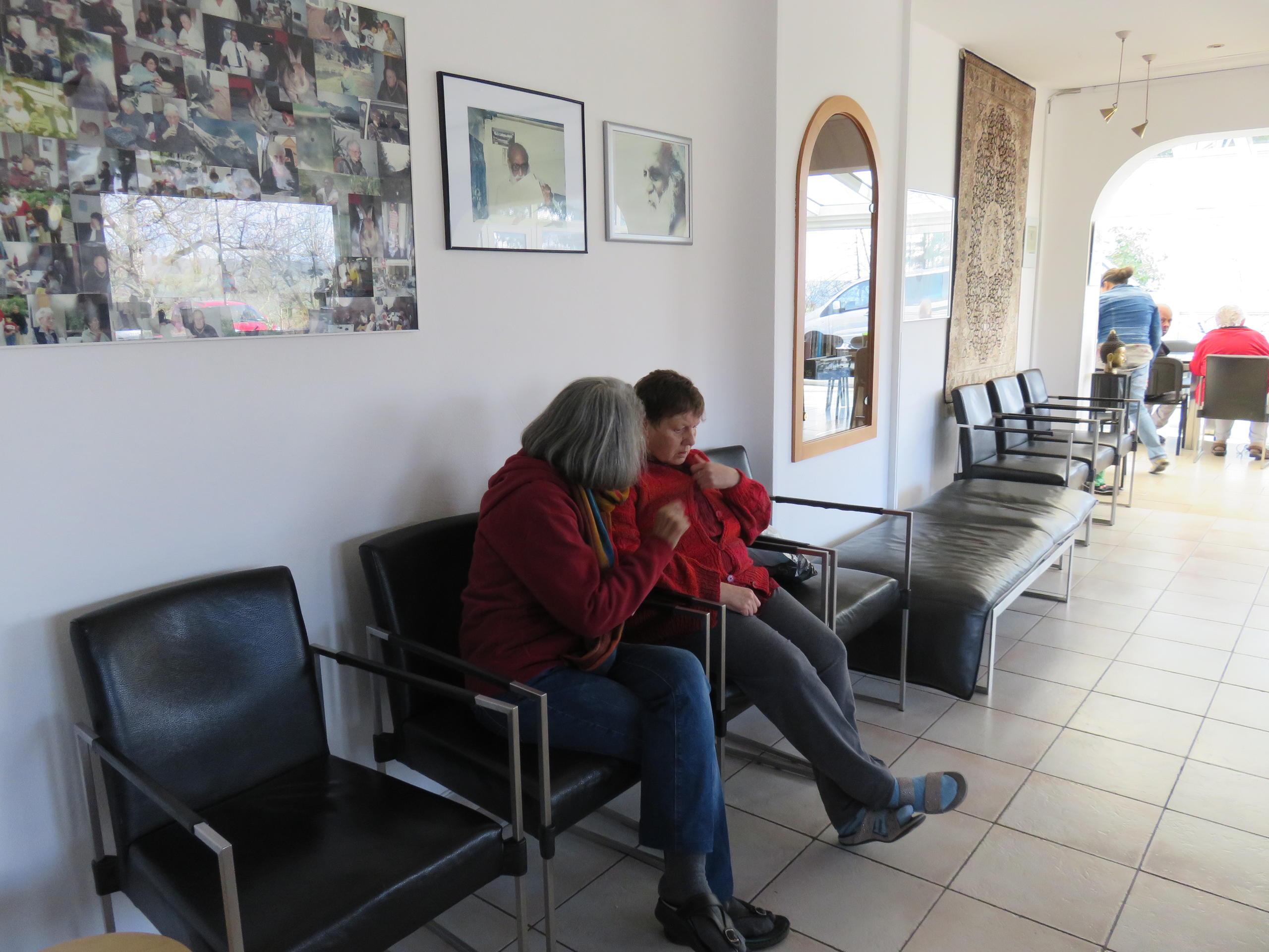 Sheela seduta su una sedia di fianco a una paziente, mentre le parla.