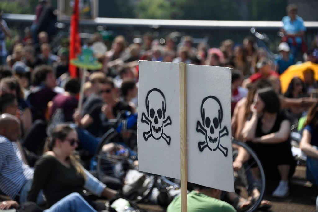 demonstrators gather, holding placard with skull and crossbones