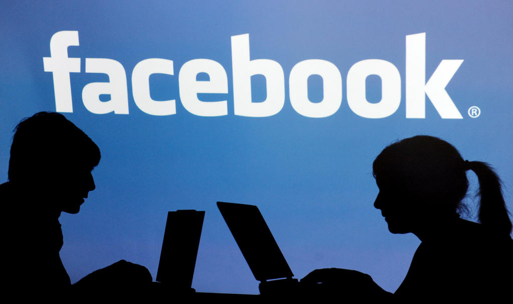 l ombra di due persone al computer e sullo sfondo la scritta facebook