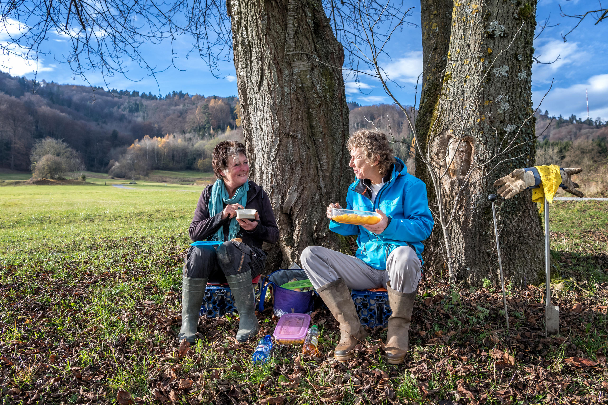 Zwei Frauen sitzen unter einem Baum am Essen