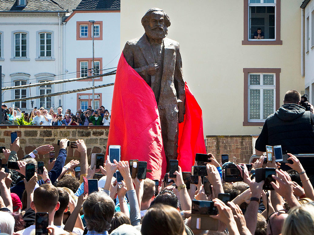 Statua in bronzo di Max ancora parzialmente coperta da velo rosso; la folla tutt attorno gira video coi telefonini