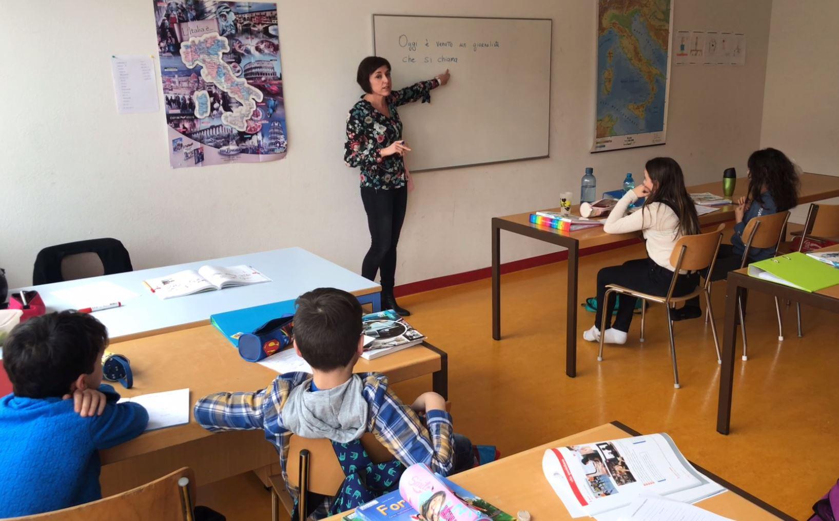 ragazzi seduti in una classe guardano la maestra che indica una frase scritta sulla lavagna