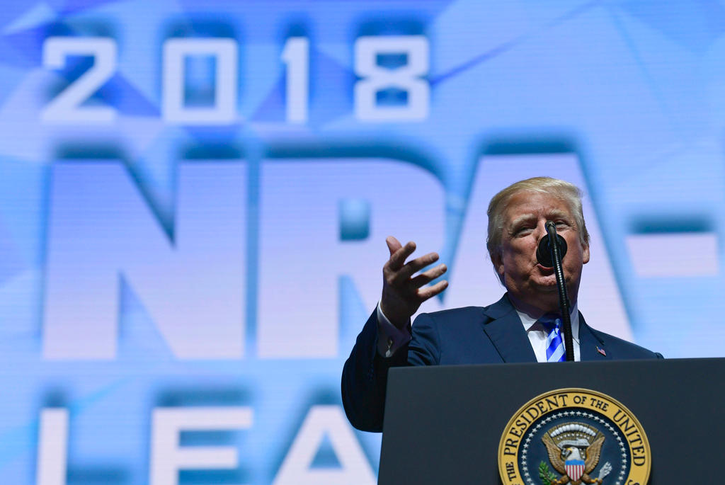 Donald Trump parla dal pulpito con lo stemma presidenziale, sullo sfondo maxi-schermo con scritta 2018 NRA