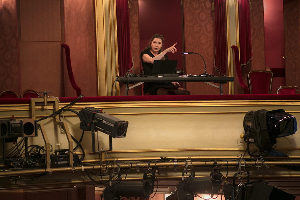 woman sits at a desk in theatre, pointing her finger to the left.