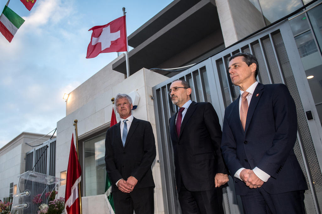 ثلاثة رجال يقفون أمام مبنى رفع عليه علم سويسرا
