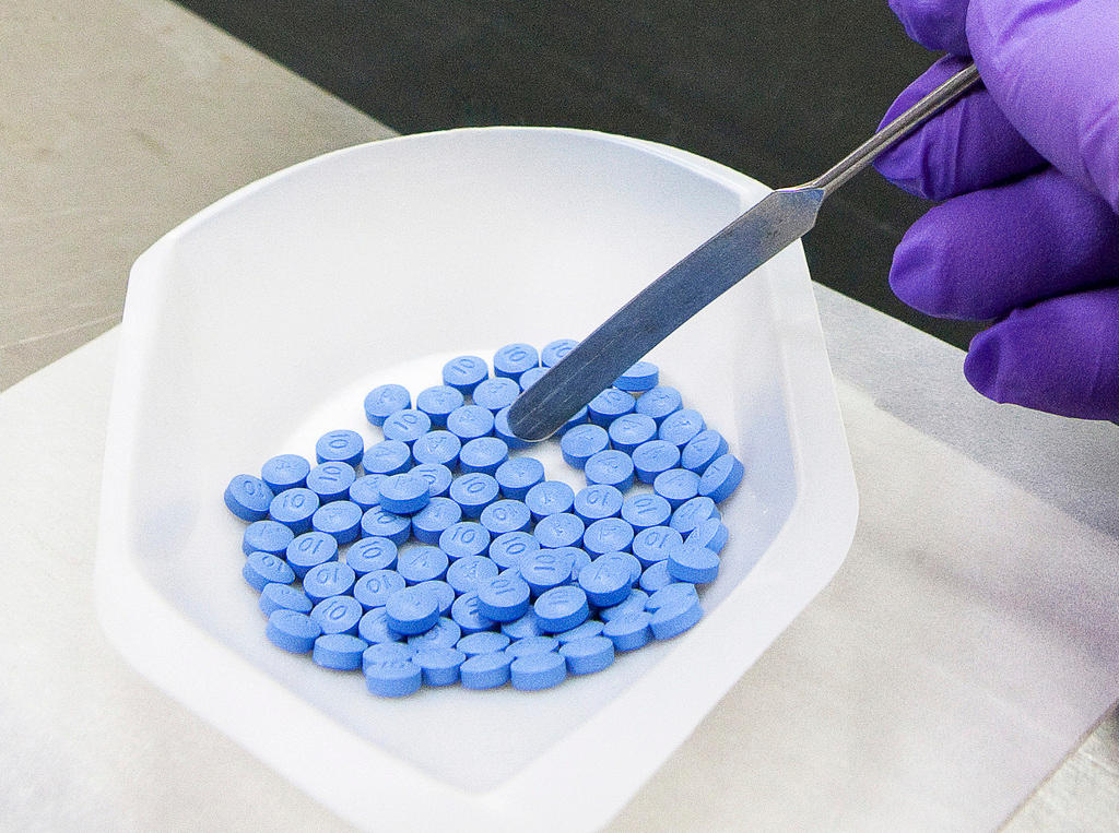 A gloved hand using an instrument to separate blue pills