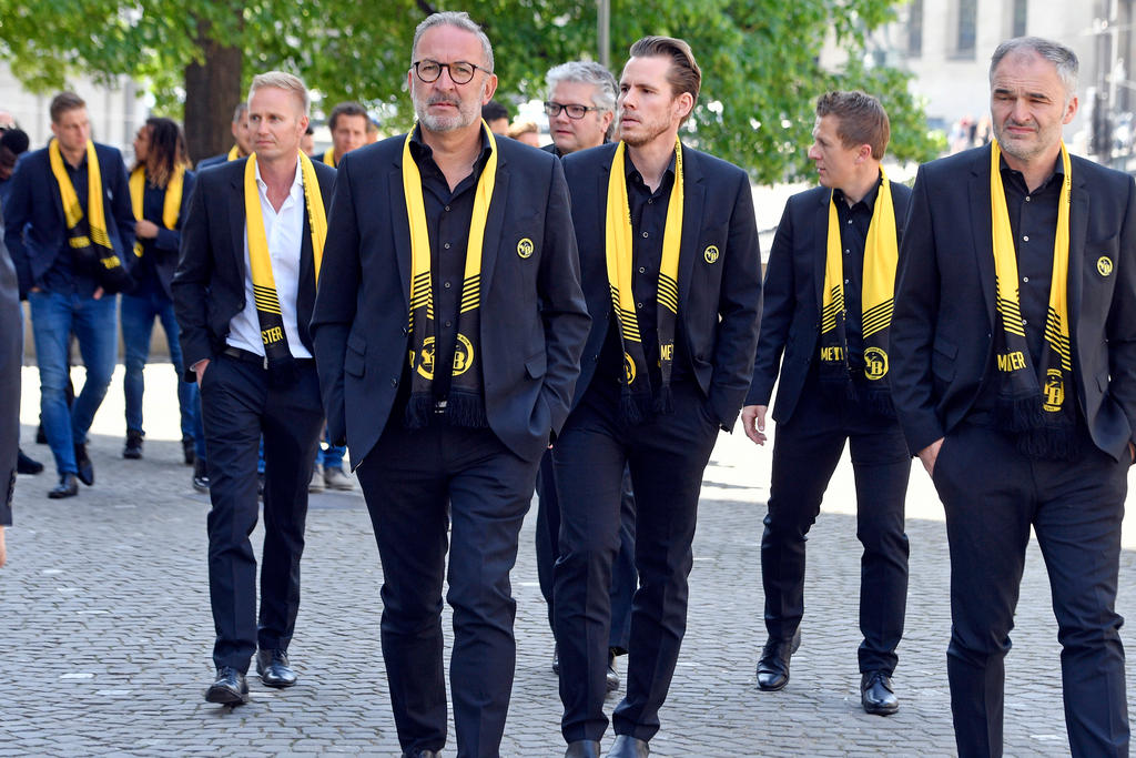 Männer mit gelben Halstüchern in schwarzen Anzügen an einer Trauerfeier