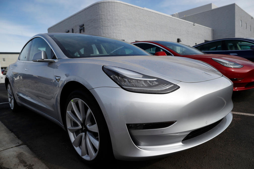 Primo piano di due automobili Tesla, una grigia una rossa, parcheggiate fuori da quello che appare come un concessionario