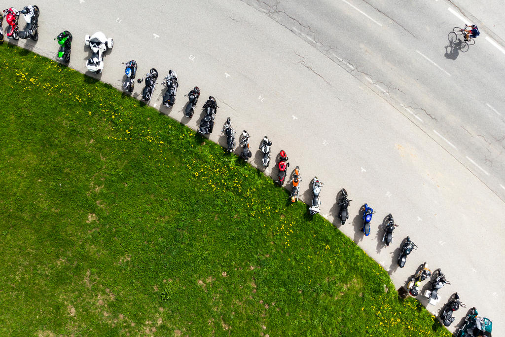 Luftaufnahme, Fahrradfahrer fährt an den parkierten Motorrädern vorbei