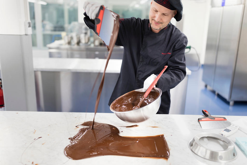 Chocolate maker pours liquid chocolate onto a table