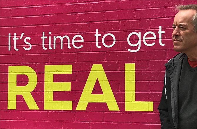 Bruno Kaufmann in front of a mural that reads: It s time to get REAL