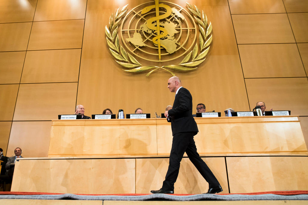 Alain Berset cammina da dx verso sx davanti al pulpito dell assemblea; sulla parete l effigie dell OMS