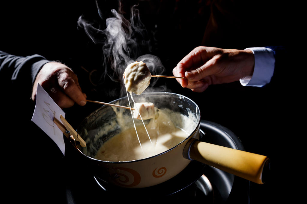 Immagine di un caquelon (pentola di terracotta) e forchettine che intingono cubetti di pane nel formaggio fuso
