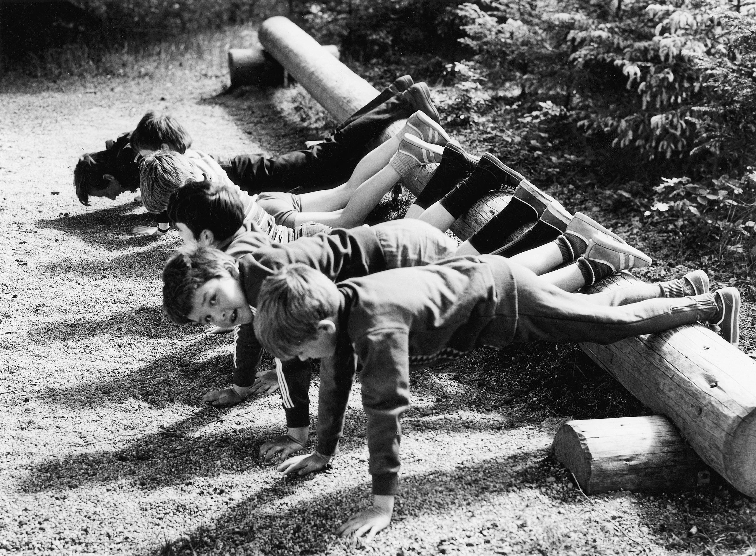 A group of boys doing push ups, feet propped onto a log