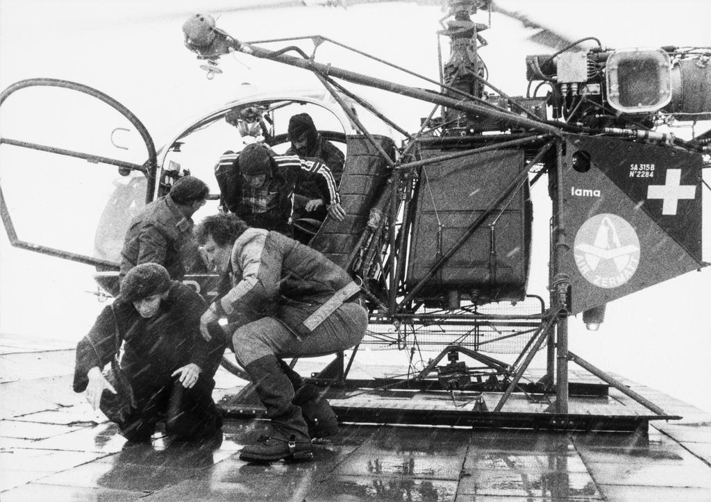 Black and white photo: A group of people leave a helicopter