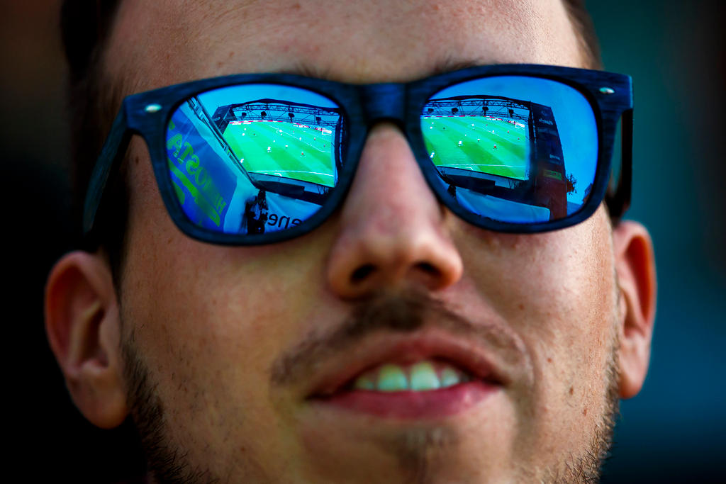 Fussballfan schaut Match auf Grossleinwand, die sich doppelt in seiner Sonnenbrille spiegelt