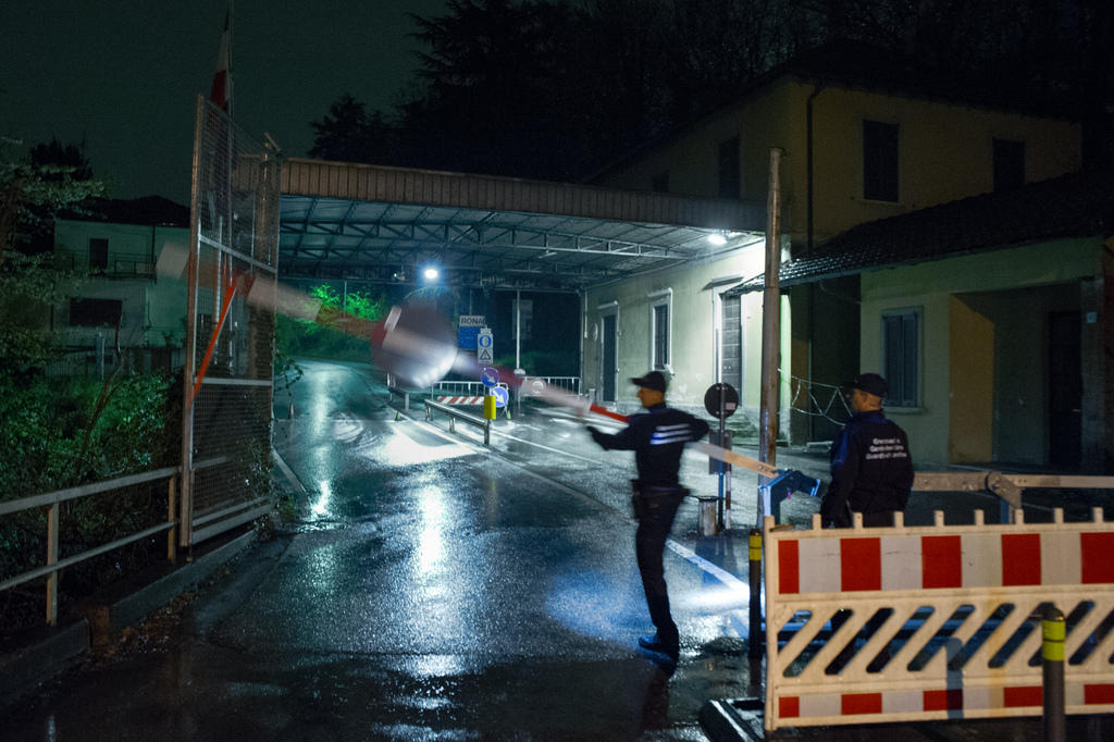 Immagine di un posto di frontiera, illuminato di notte, con due guardie di confine che abbassano una barriera