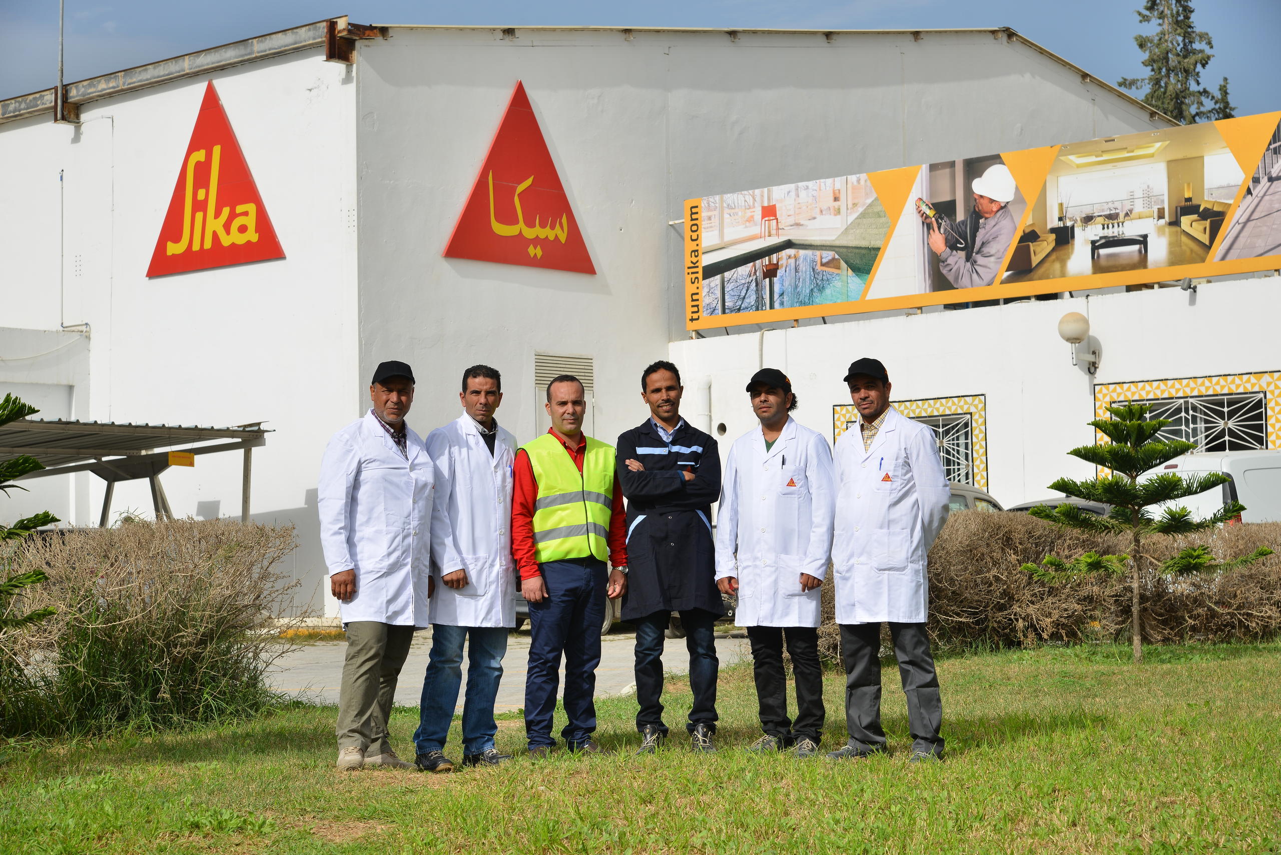 صورة جماعية لست رجال بملابس العمل أمام مصنع تابع لشركة سويسرية في تونس