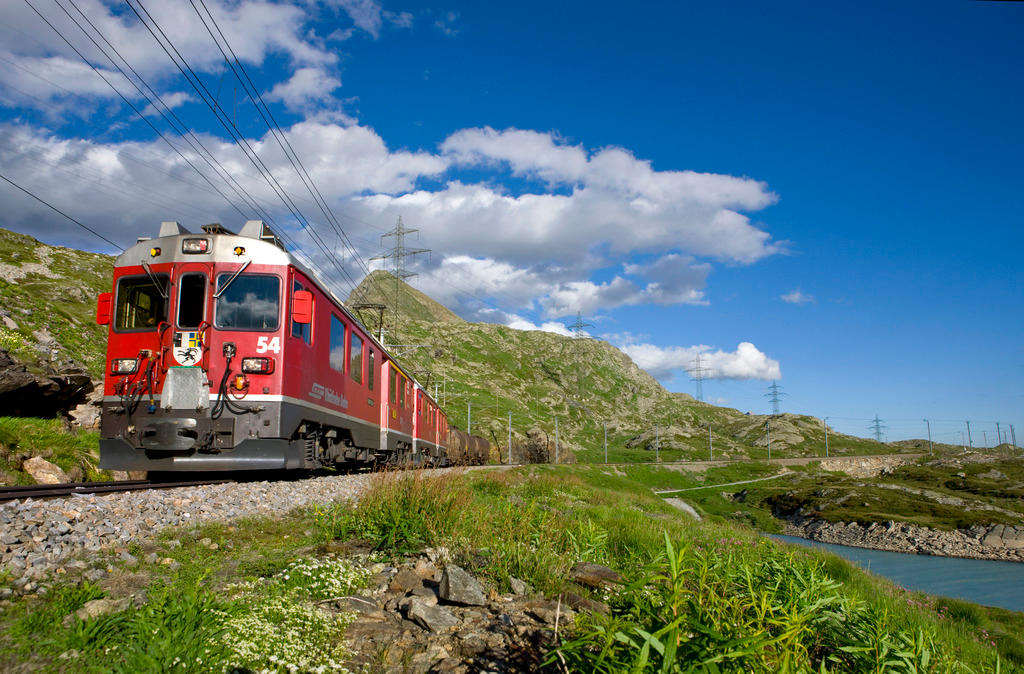 Trenino visto quasi frontalmente, diretto verso l obiettivo in un paesaggio di montagna con laghetto e cielo terso