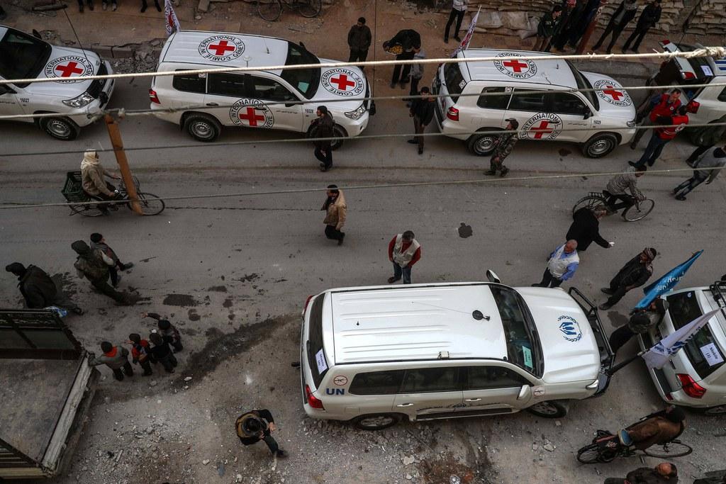 People gather near UN and ICRC cars in a street in Douma, Syria.