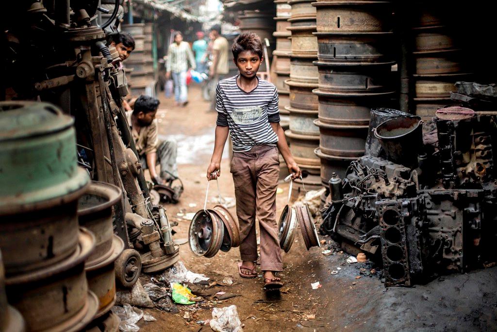 Indian child carrying metal wheels at an automobile reycle market in Calcutta.