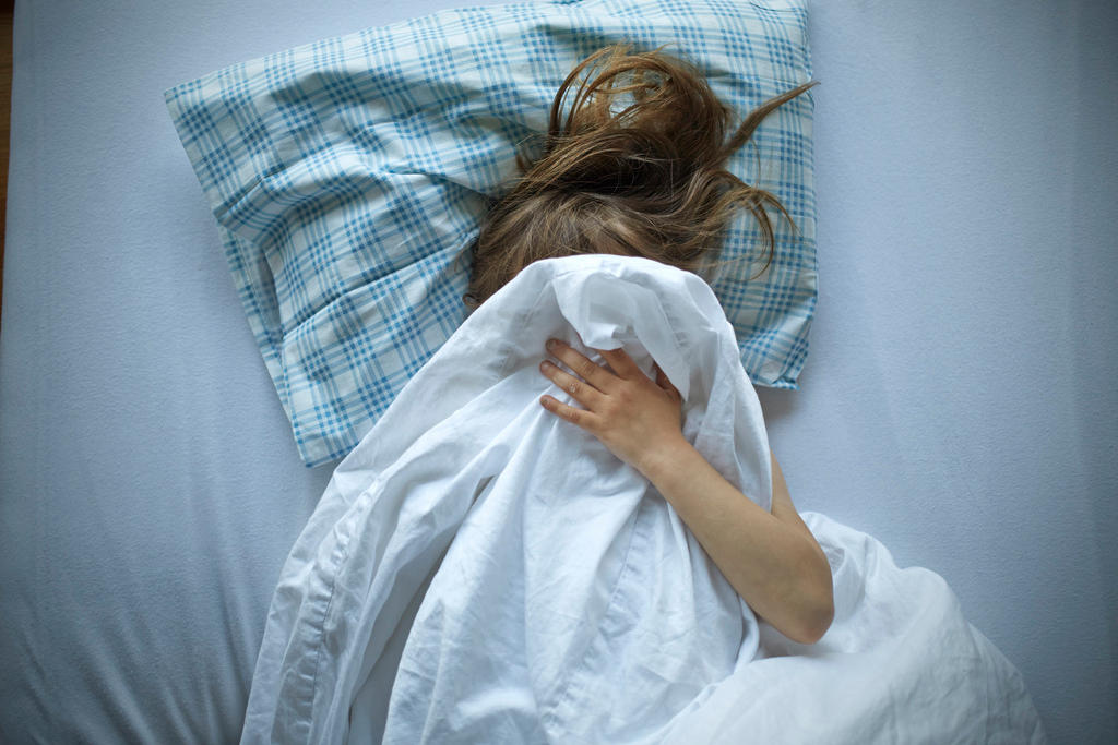 Una niña en su cama, aparentemente asustada, se tapa la cara.