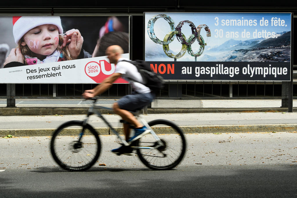 Velofahrer fährt vor zwei Plakaten pro und kontra Sion 2026 durch.