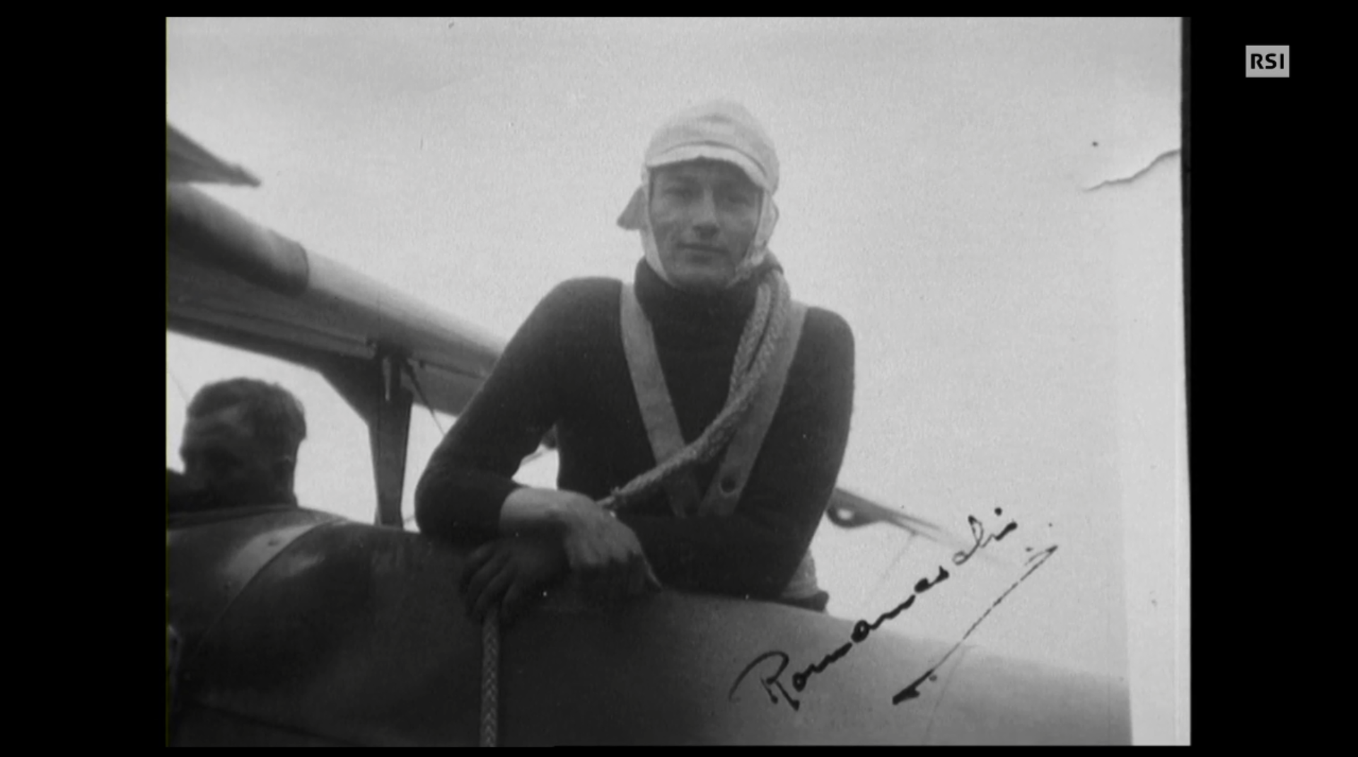 Riproduzione di cartolina con uomo che guarda in camera, appoggiato sull ala di un piccolo aereo.